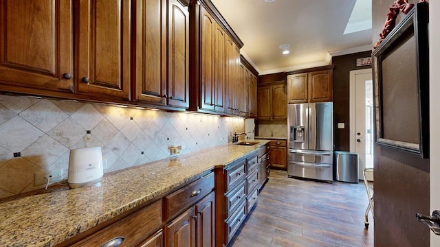 kitchen featuring stainless steel fridge with ice dispenser, a sink, light stone countertops, light wood-type flooring, and tasteful backsplash