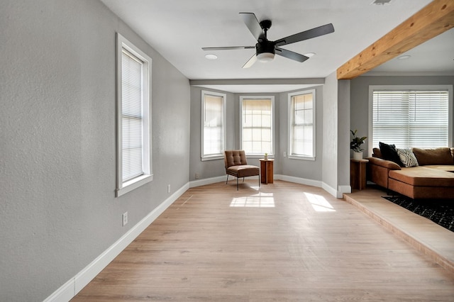 sitting room with baseboards, ceiling fan, light wood-style flooring, and a textured wall