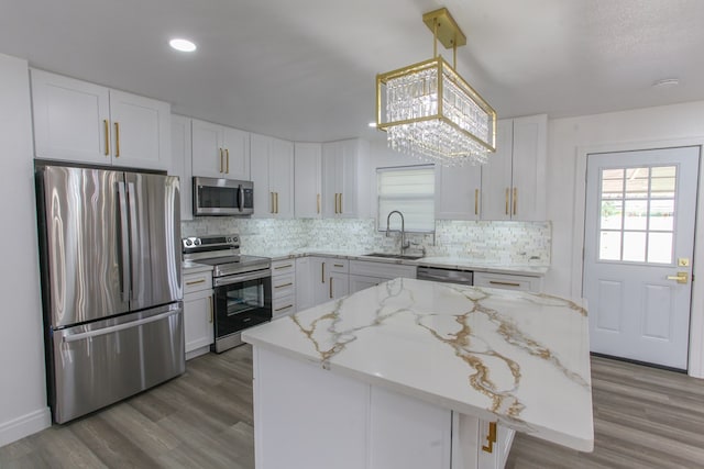 2702 Ann Dr, Big Spring, TX 79720 - kitchen with appliances with stainless steel finishes, backsplash, a kitchen island, white cabinetry, and wood finished floors