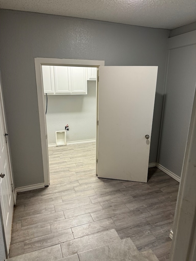 empty room with a textured ceiling, baseboards, and light wood-style flooring