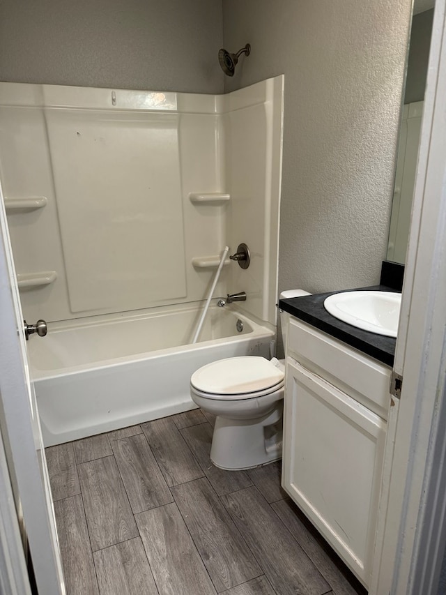bathroom with shower / bathing tub combination, wood finished floors, vanity, toilet, and a textured wall