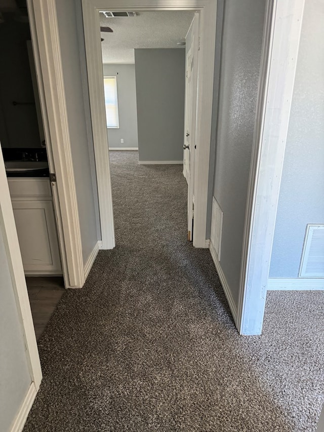 hall featuring baseboards, a textured ceiling, and visible vents