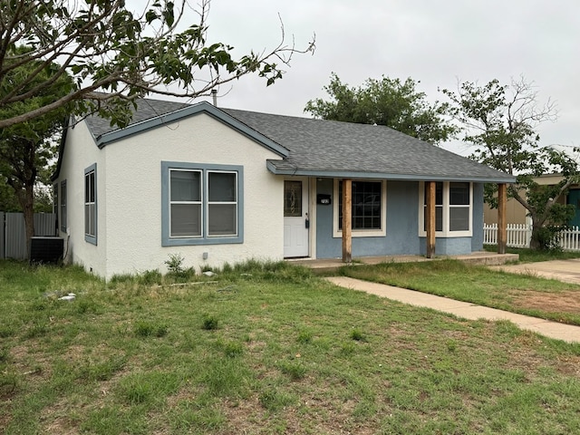 view of front of house with covered porch, a front yard, fence, and roof with shingles