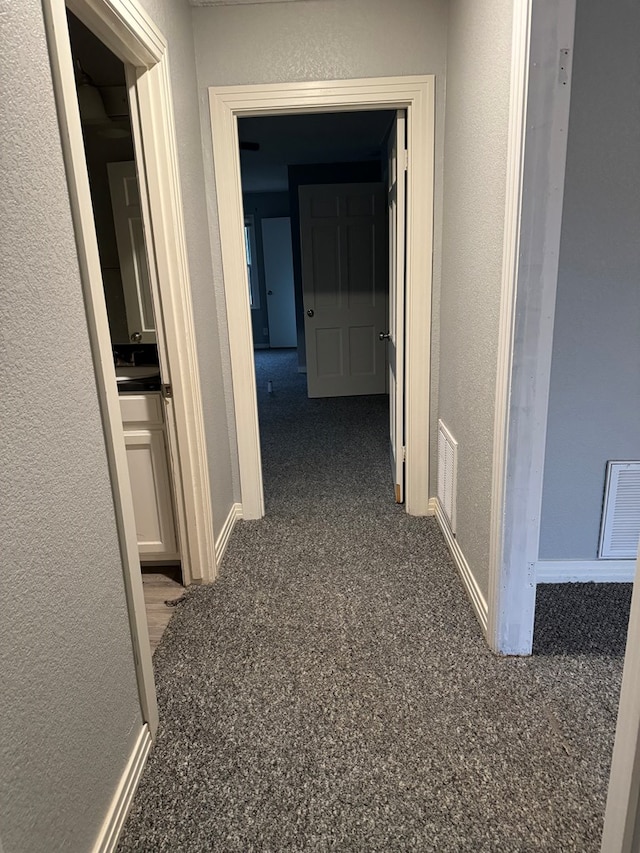 corridor featuring a textured wall, visible vents, and baseboards