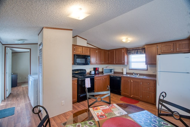 kitchen with lofted ceiling, black appliances, sink, a textured ceiling, and light hardwood / wood-style floors