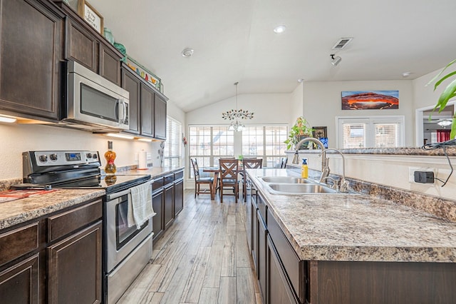 kitchen with an island with sink, sink, stainless steel appliances, dark brown cabinets, and light hardwood / wood-style flooring