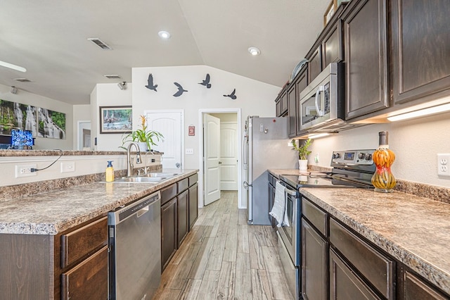 kitchen with sink, appliances with stainless steel finishes, dark brown cabinets, light hardwood / wood-style floors, and vaulted ceiling