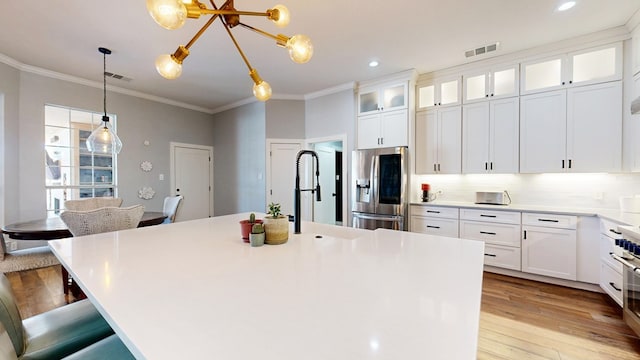 kitchen with a breakfast bar area, light wood-style flooring, stainless steel appliances, visible vents, and ornamental molding