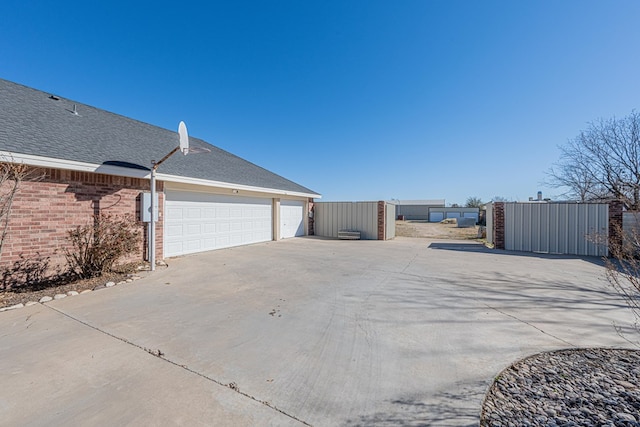 view of side of home with roof with shingles, a detached garage, fence, and brick siding