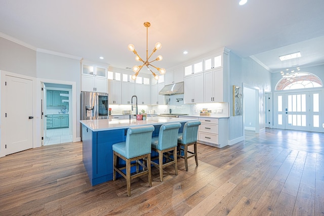 kitchen featuring an inviting chandelier, under cabinet range hood, crown molding, and stainless steel fridge with ice dispenser