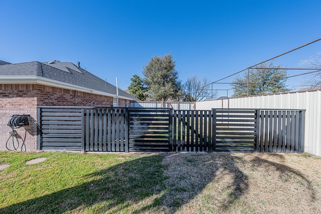 view of gate with a fenced backyard and a lawn