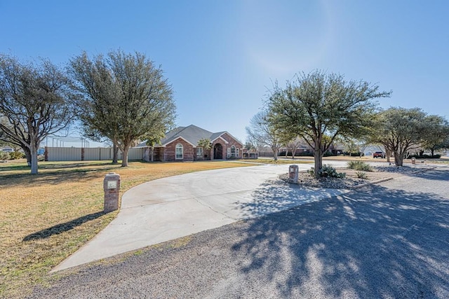 view of front of house featuring fence, curved driveway, and a front lawn