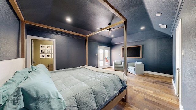 bedroom with lofted ceiling, a textured wall, baseboards, and wood finished floors