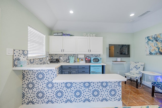 kitchen with tasteful backsplash, light countertops, visible vents, white cabinets, and a peninsula