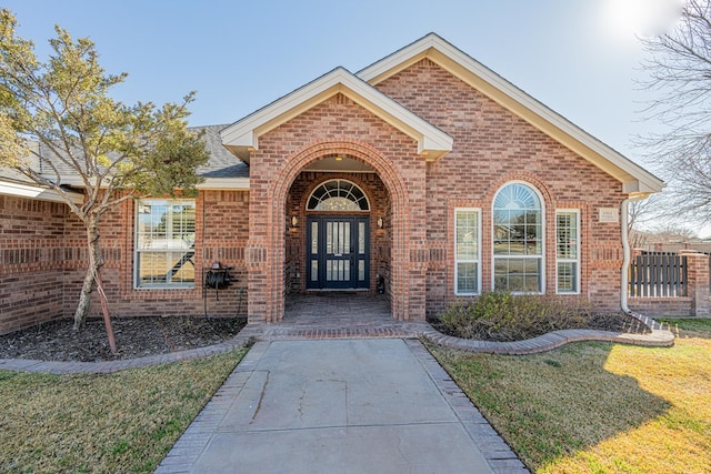 entrance to property with a shingled roof, brick siding, and a lawn