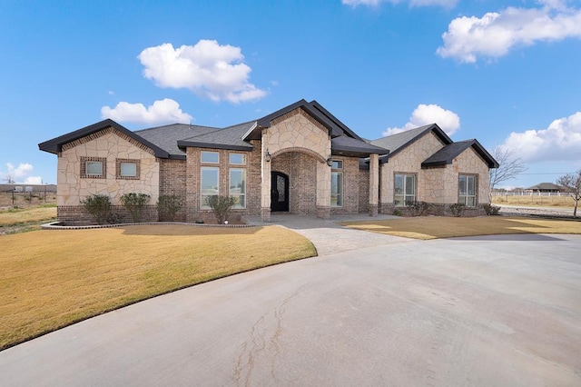 7704 W County Rd 52 Unit A, Midland, TX 79707 - french country home with stone siding, a front yard, brick siding, and roof with shingles