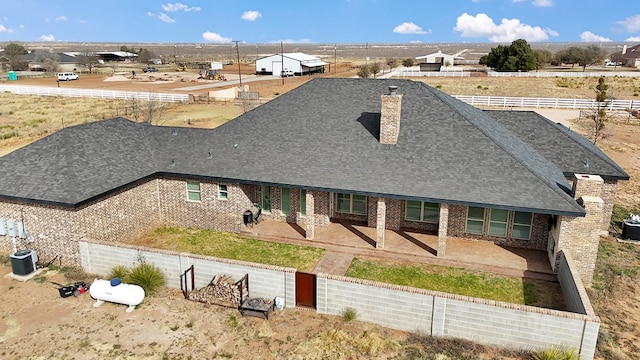 7704 W County Rd 52 Unit A, Midland, TX 79707 - view of front of house featuring cooling unit, a shingled roof, brick siding, a patio, and a chimney