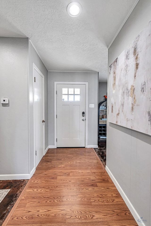 foyer entrance with a textured ceiling, baseboards, and wood finished floors