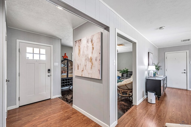 foyer entrance with visible vents, a textured ceiling, ornamental molding, and wood finished floors