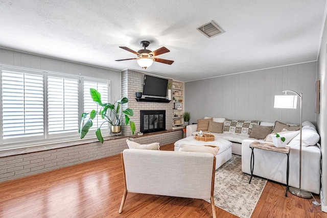 living area with ceiling fan, visible vents, a fireplace, and wood finished floors