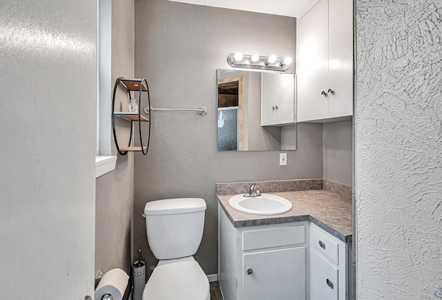 bathroom featuring a textured wall, vanity, and toilet