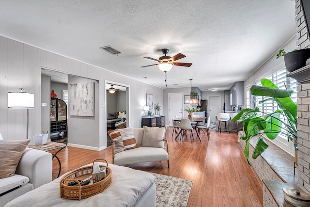 living area featuring light wood finished floors, visible vents, a ceiling fan, a textured ceiling, and baseboards