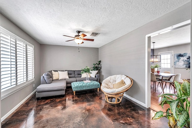 living room featuring baseboards, visible vents, a textured ceiling, concrete floors, and ceiling fan with notable chandelier