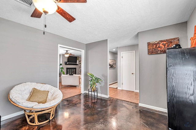 living area featuring finished concrete flooring, a brick fireplace, baseboards, and a textured ceiling