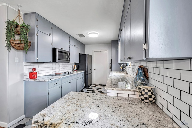 kitchen with visible vents, decorative backsplash, gray cabinetry, appliances with stainless steel finishes, and a sink