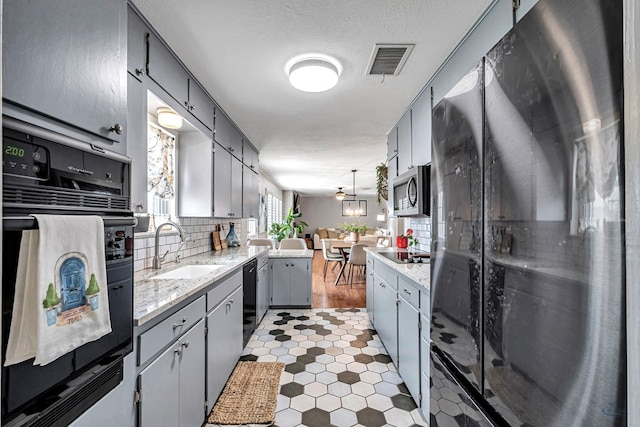 kitchen with tasteful backsplash, visible vents, gray cabinets, black appliances, and a sink