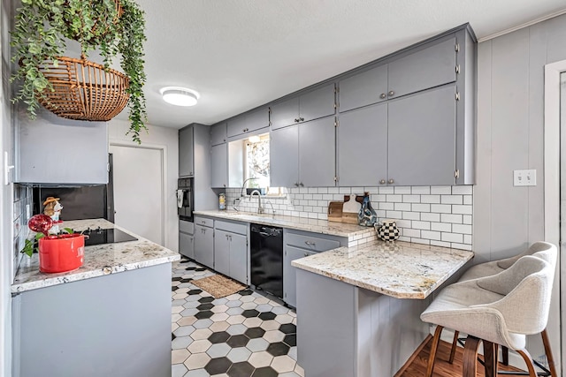 kitchen featuring a peninsula, a kitchen breakfast bar, gray cabinets, black appliances, and tasteful backsplash