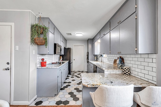 kitchen with stainless steel appliances, a peninsula, visible vents, gray cabinets, and tasteful backsplash