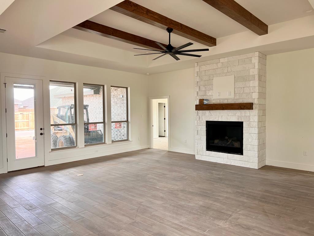 unfurnished living room with beam ceiling, wood finished floors, a ceiling fan, baseboards, and a stone fireplace