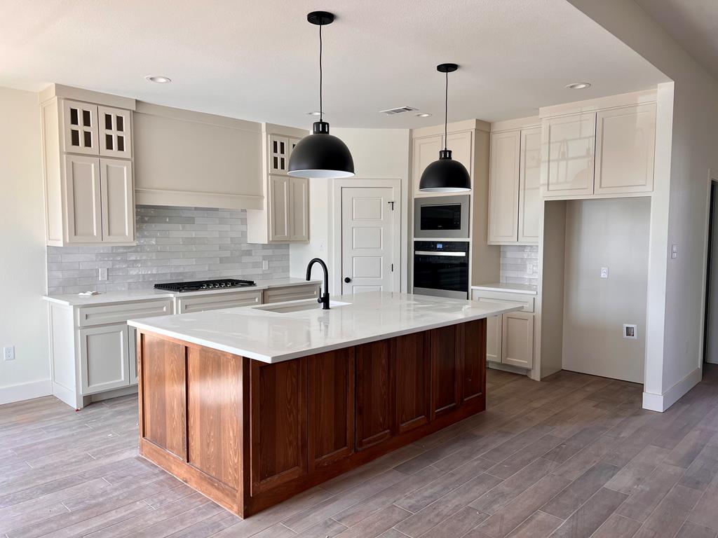 kitchen featuring a sink, black oven, stainless steel microwave, light countertops, and tasteful backsplash