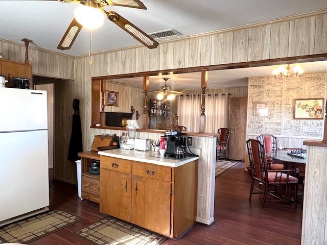 3702 Dalton Dr, Snyder, TX 79549 - kitchen with freestanding refrigerator, visible vents, ceiling fan with notable chandelier, wood walls, and dark wood-type flooring