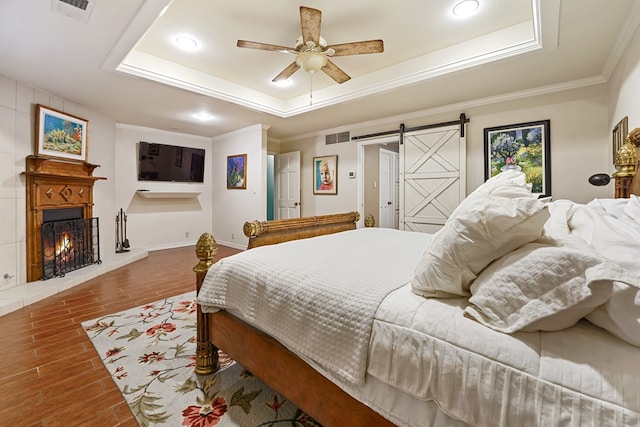 bedroom with crown molding, a barn door, ceiling fan, and a tray ceiling