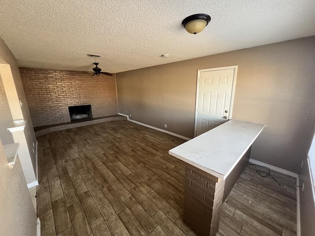 unfurnished living room with ceiling fan, brick wall, dark hardwood / wood-style floors, a textured ceiling, and a fireplace