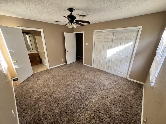 unfurnished bedroom with connected bathroom, ceiling fan, a textured ceiling, light carpet, and a closet