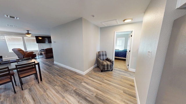 hall featuring attic access, light wood-type flooring, visible vents, and baseboards