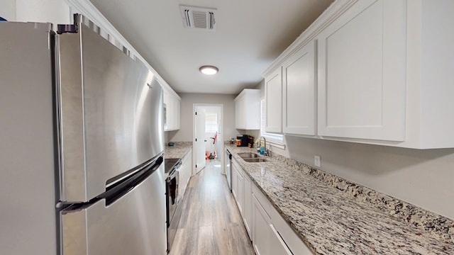 kitchen featuring a sink, visible vents, white cabinets, light wood-style floors, and appliances with stainless steel finishes