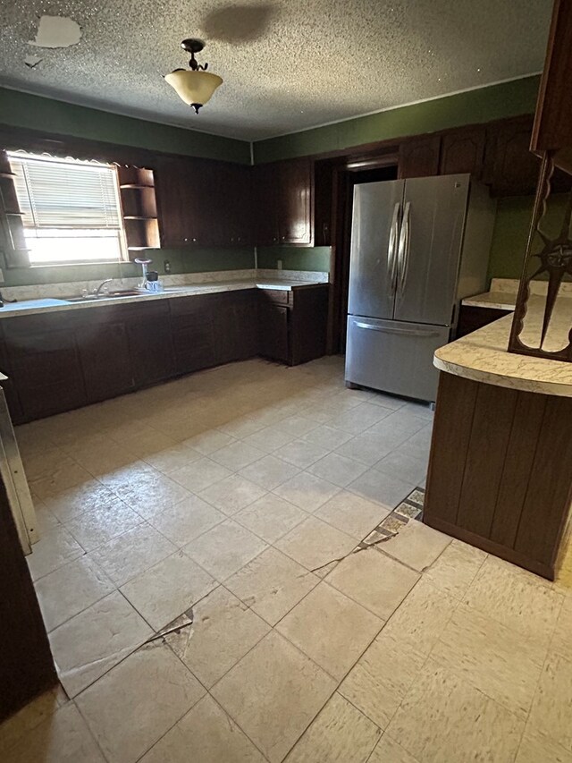 kitchen featuring dark brown cabinets, a textured ceiling, and stainless steel refrigerator