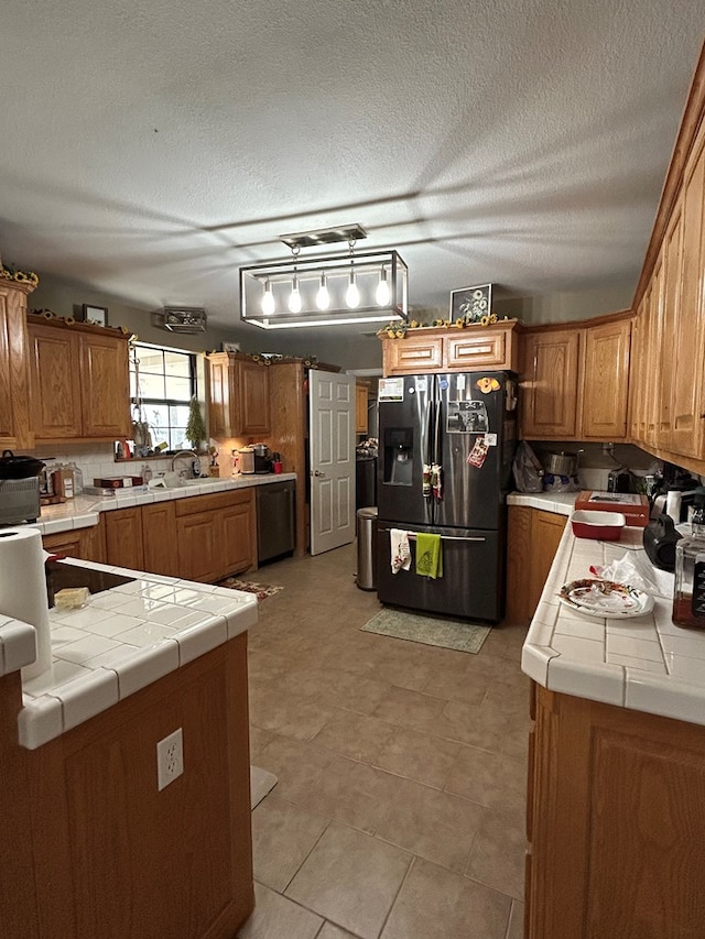 kitchen with tile countertops, pendant lighting, a textured ceiling, light tile patterned floors, and appliances with stainless steel finishes