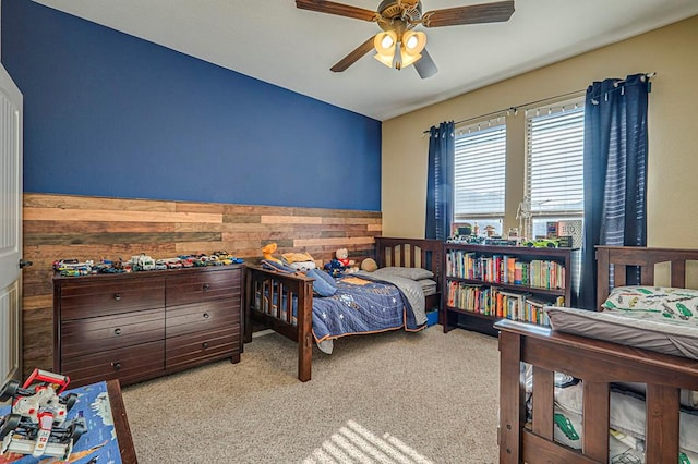 carpeted bedroom with ceiling fan and wood walls