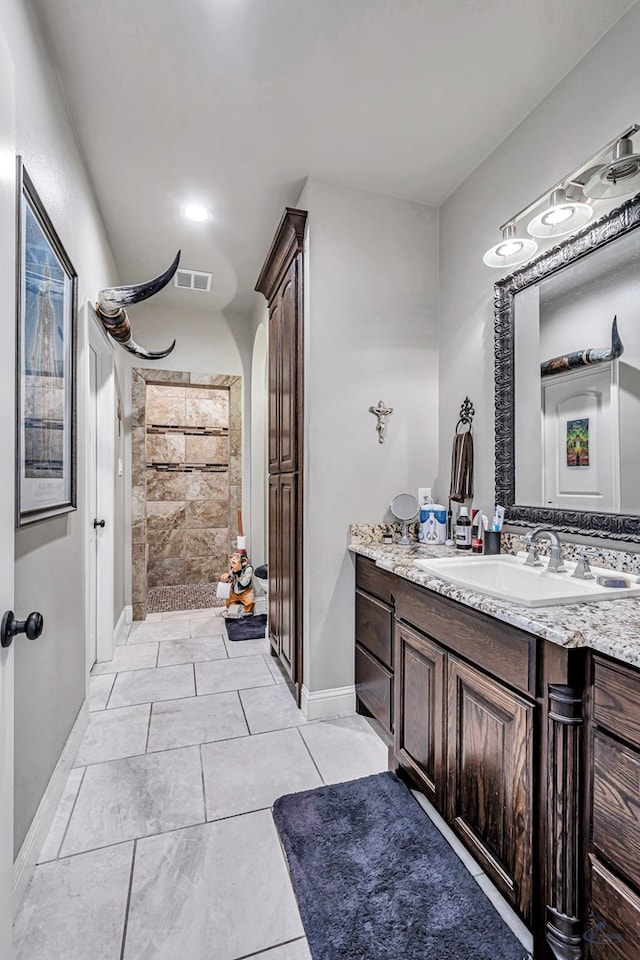 full bathroom featuring tiled shower, vanity, visible vents, and baseboards