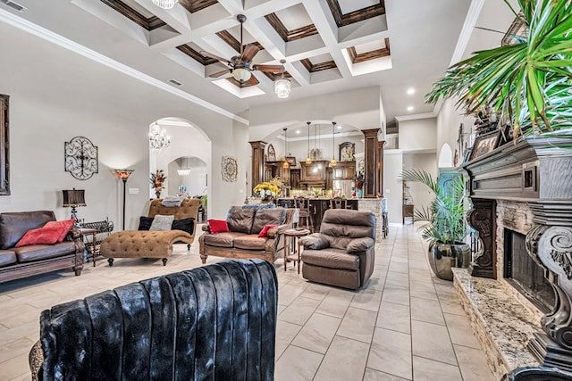 living room with arched walkways, a high ceiling, ceiling fan, a stone fireplace, and ornate columns