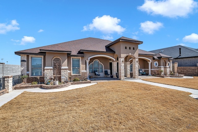 view of front facade with fence, stone siding, roof with shingles, stucco siding, and a front lawn