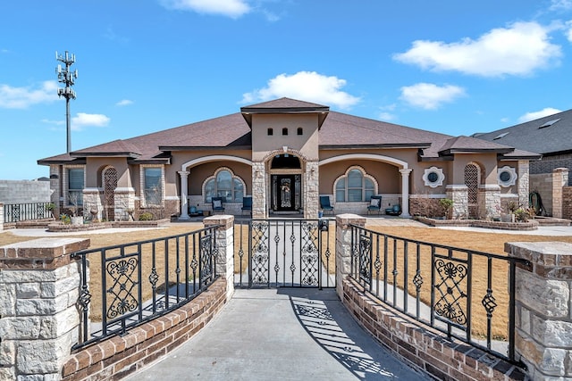exterior space with stone siding, a fenced front yard, a gate, and stucco siding