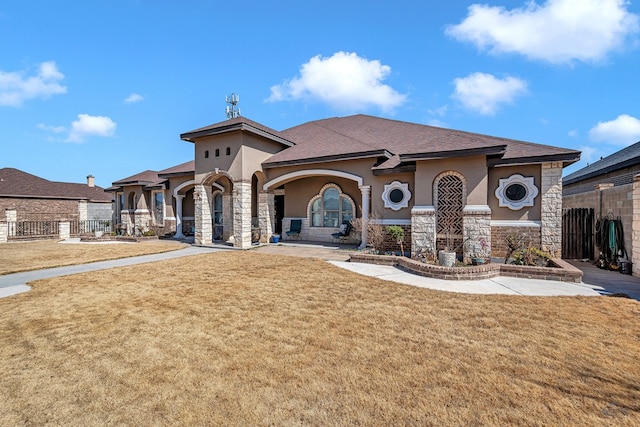 mediterranean / spanish-style house featuring stone siding, fence, and stucco siding