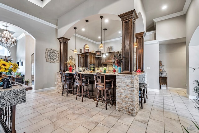 kitchen featuring decorative columns, a breakfast bar area, light stone counters, and dark brown cabinets