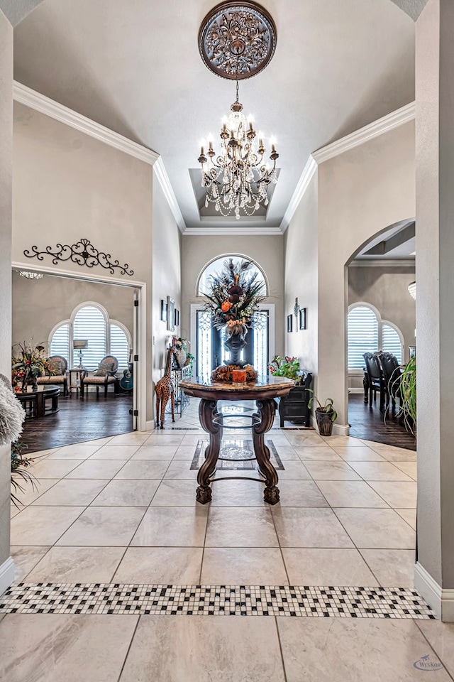 tiled foyer entrance with a towering ceiling, an inviting chandelier, ornamental molding, and a wealth of natural light